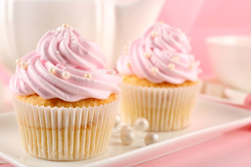 Two tasty pink cupcakes and teapot, closeup