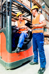 Workers in logistics warehouse at forklift checking list