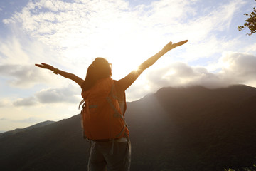 cheering woman open arms at sunrise mountain peak