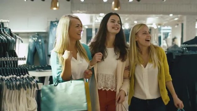 Three happy girls are walking through a clothing store in colorful garments. Shot on RED Cinema Camera.
