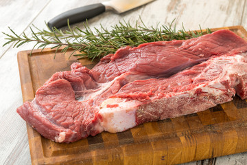 Fetta di carne rossa cruda e rosmarino sul tagliere di legno  con mannaia da cucina