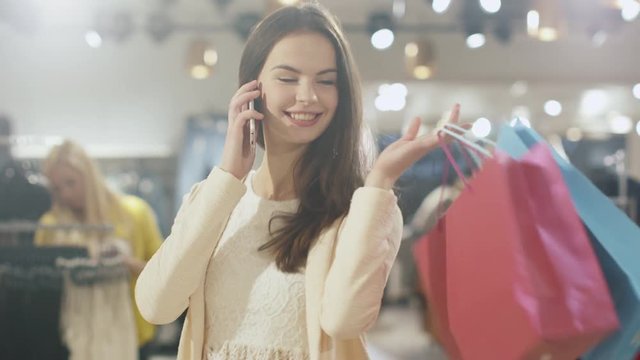Cheerful young brunette girl is walking though a clothing store while talking on the phone. Shot on RED Cinema Camera.