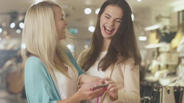 Two young happy girls are using a smartphone in a department store. Shot on RED Cinema Camera.
