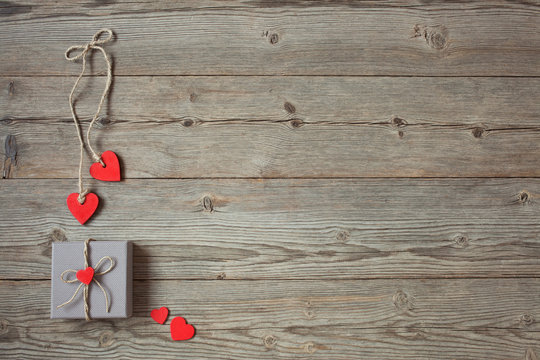 Wooden background with a gift in a box and red hearts on Valentine's Day