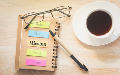 mission text on a Post-it with glasses and pen. And a glass coffee table. Vintage tone.