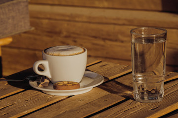 Cappuccino coffee in a white cup. with cinnamone and biscuits.in a glass of water.Coffee flavored drink, cappuccino is made of Italian espresso. It is very fragrant and delicious drink.