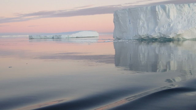 Sailing through calm waters of Antarctic Sound, Antarctica with field of tabular icebergs at sunset.
