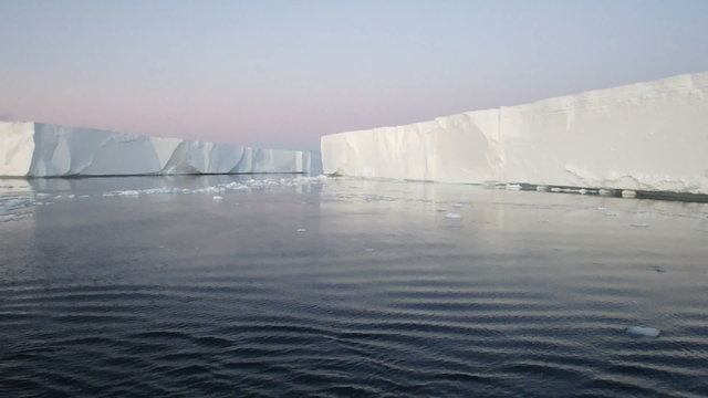 Sailing through calm waters of Antarctic Sound, Antarctica with field of tabular icebergs at sunset.
