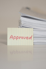 Approved; Stack of Documents on white desk and Background.