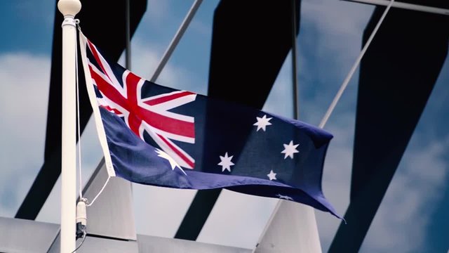Australian Flag with wind in slow motion and blue sky reflections