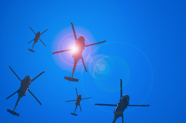 A large squadron of United States military helicopters flying over with the sun bursting out of the edge of the leading helicopter