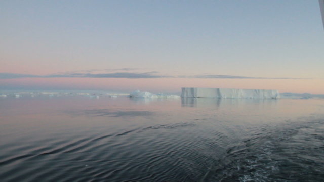 Sailing through calm waters of Antarctic Sound, Antarctica with field of tabular icebergs at sunset.

