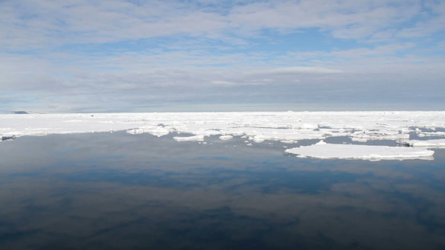 Passenger ship moving through field of pack ice with reflection of clouds in calm waters of Antarctic Sound in Antarctica.
