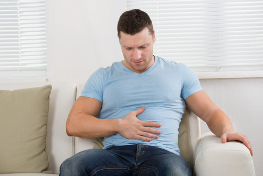 Man With Stomach Ache Sitting On Couch At Home