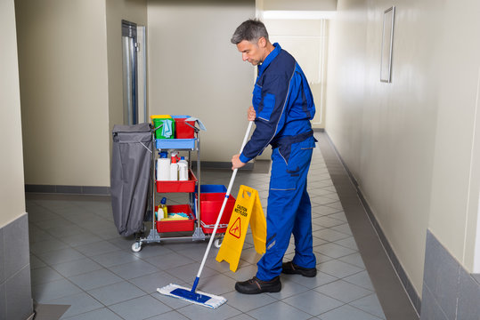 Male Worker With Broom Cleaning Corridor