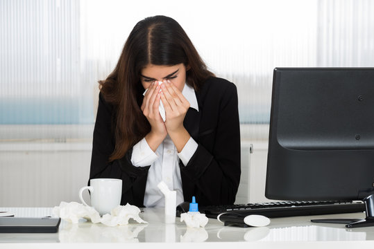 Sick Businesswoman Blowing Her Nose At Desk In Office