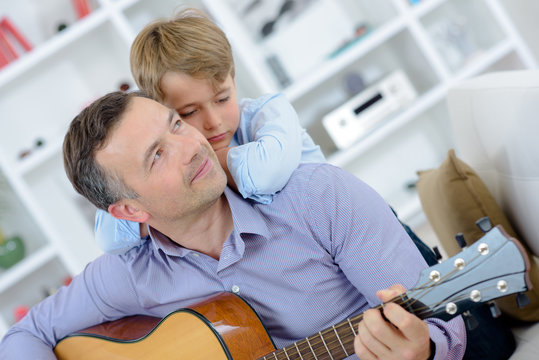 Man playing guitar, boy leaning on his shoulders