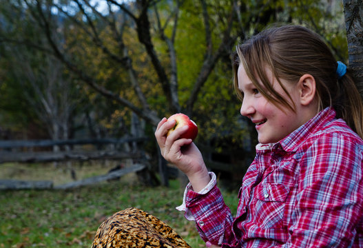 Little girl sitting outdoor nad eating an apple