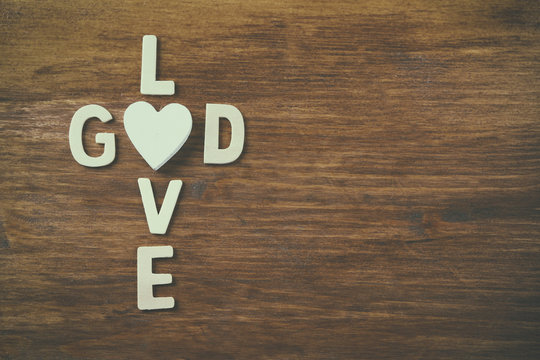 selective focus photo of The words love is god made with block wooden letters on wooden background. religion concept