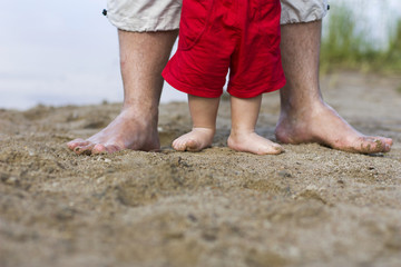 Fototapeta na wymiar Feet of dad and child on the sand near the lake