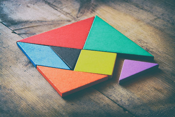 a missing piece in a square tangram puzzle, over wooden table. 