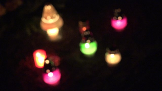 Cemetery at night with colorful candles for All Saints Day. All Saints Day is a solemnity celebrated on 1 November by Catholic Church. Focus blur out shot. 4K
