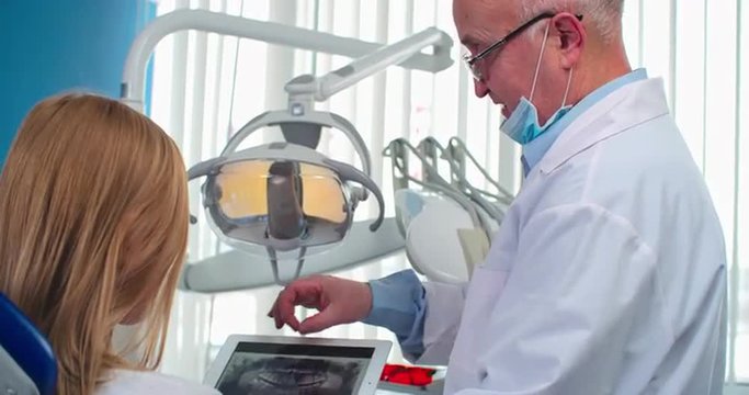 Mature dentist showing x-ray picture of teeth of his patient and telling which problems she has