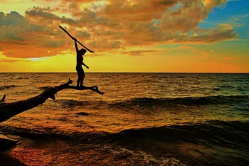 Fotobehang The Hunt. Silhouette of a male balanced on a log over the water preparing to spear a fish. © ehrlif