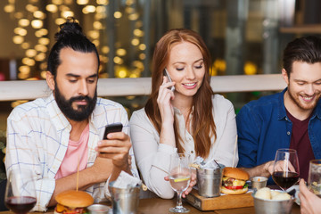 happy friends with smartphones at restaurant