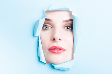 Young woman face looking thru torn cardboard