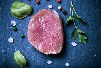 Raw meat with herbs and spices on a black slate plate. Toned