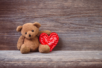 Teddy bear with heart sitting on old wood background.