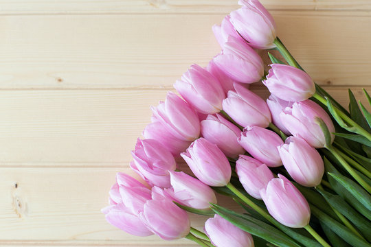 bouquet of pink tulips lie on natural wooden textur table wrapped in Kraft paper