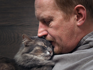 Portrait of a man with a cat. Large man's face and muzzle cat. Man tenderly, lovingly kisses the cat. Male red-haired, gray cat. Man and cat