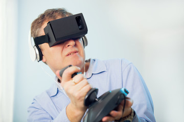 Man holding a gaming computer wheel getting experience using VR-headset glasses of virtual reality at home