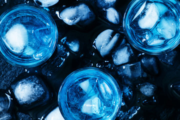 Blue cocktail with ice cubes on black stone background, top view