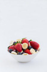 A bowlful of fruit including strawberries, blueberries and bananas. Ingredients for smoothies and juicers. Healthy ingredients. White isolated background. Portrait orientation.