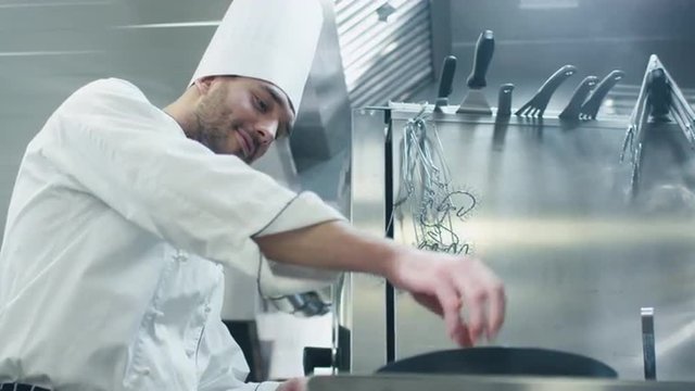 Professional chef in a commercial kitchen in a restaurant or hotel is preparing food on a pan. Shot on RED Cinema Camera.