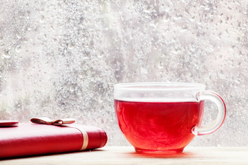 Cup with hot red tea in front of a window with water drops in ra