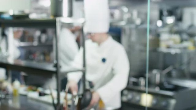 Blur footage of three professional chefs in a commercial kitchen in a restaurant or hotel preparing food. Shot on RED Cinema Camera.