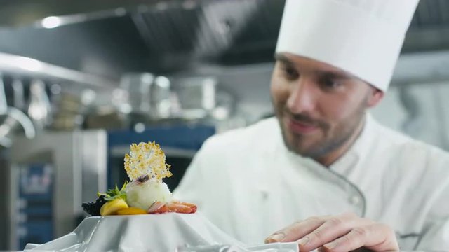 Happy professional chef in a commercial kitchen is garnishing ice cream dessert with strawberry. Shot on RED Cinema Camera.