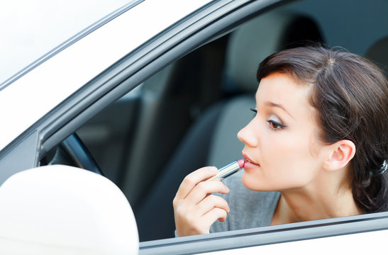 Young brunette woman applying makeup while in the car