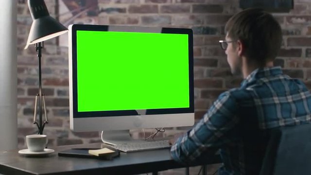 Young man is working on a computer with a mock-up green screen. Shot on RED Cinema Camera.