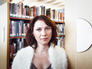 Closeup portrait of middle age mature brunette Caucasian woman student in library  looking directly in camera, teacher librarian profession, back to school concept