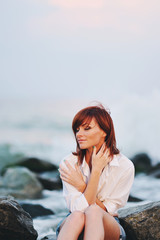 Молодая красивая девушка сидит на камнях на берегу моря 