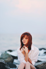 Fototapeta na wymiar Молодая красивая девушка сидит на камнях на берегу моря 