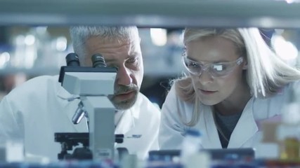 Male and female scientist are working with a microscope and a tablet in a laboratory. Shot on RED Cinema Camera. - Powered by Adobe