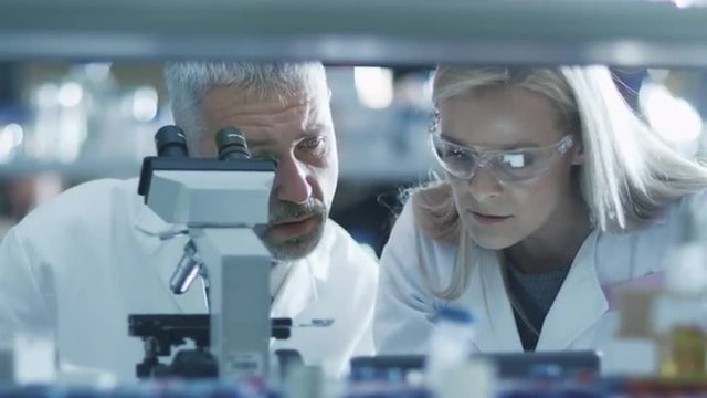 Male and female scientist are working with a microscope and a tablet in a laboratory. Shot on RED Cinema Camera.