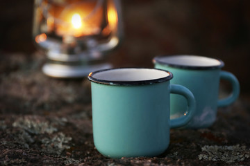 Decorative lamp and two blue mugs on rock in mountains