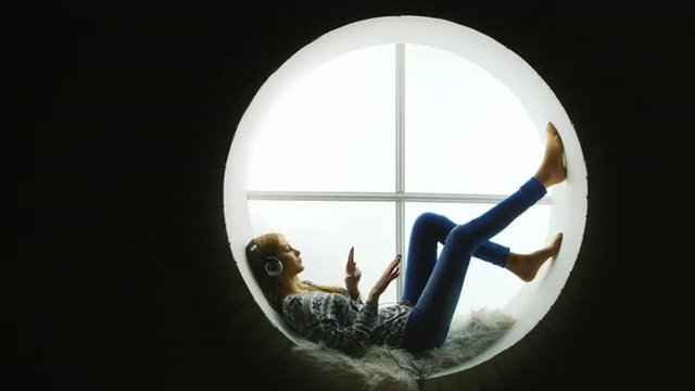 Attractive woman sitting at the round window, listening to music.
